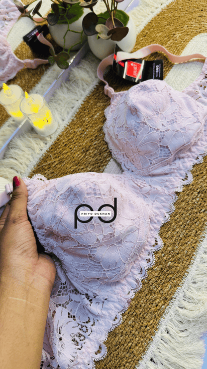 White lace bra with 'pd' branding held by a hand on a patterned surface.